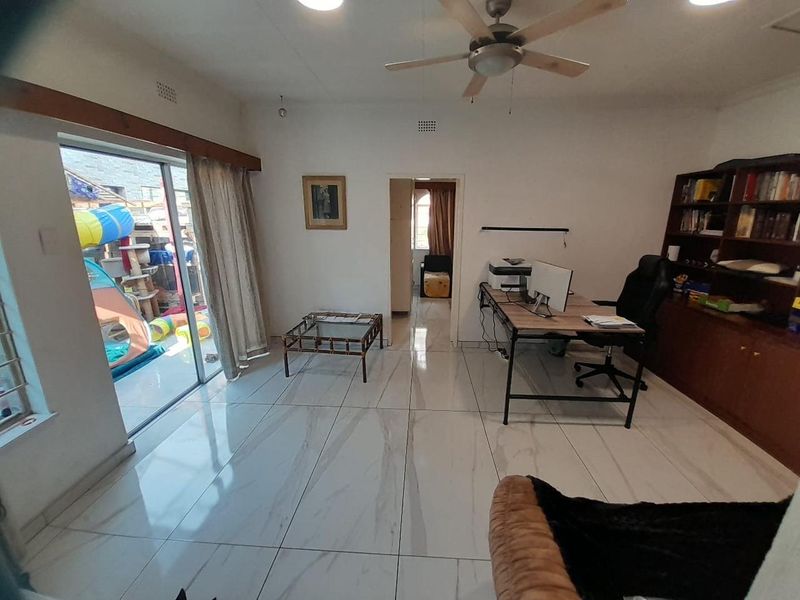 A living area featuring large format tiled flooring, a ceiling fan, and a sliding glass door providing access to the outdoor space.