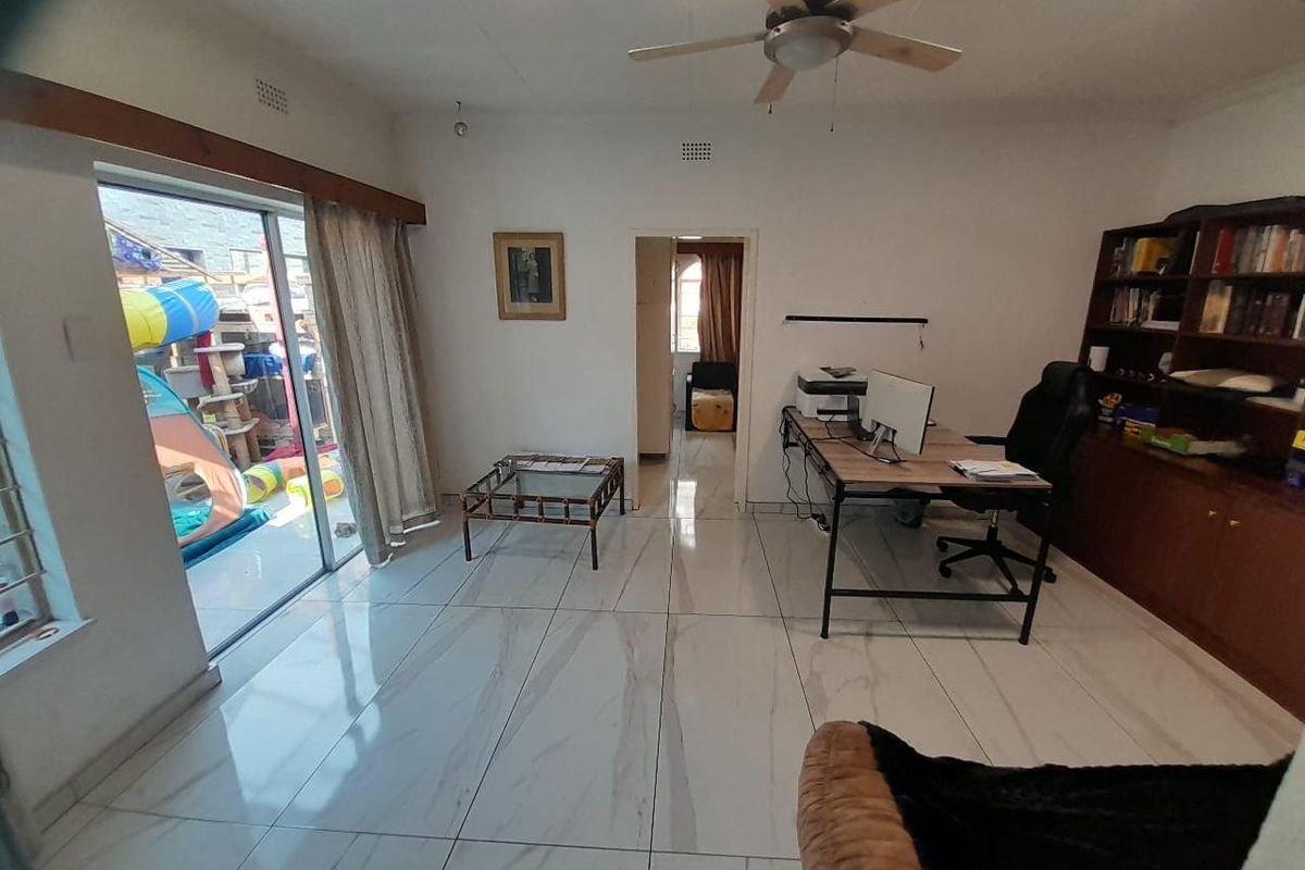 A living area featuring large format tiled flooring, a ceiling fan, and a sliding glass door providing access to the outdoor space.