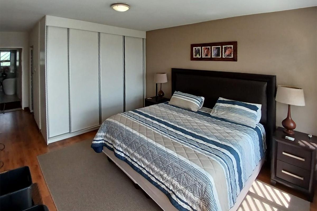 A spacious bedroom featuring built-in floor-to-ceiling wardrobes, laminate flooring, and a flush-mount ceiling light fixture.