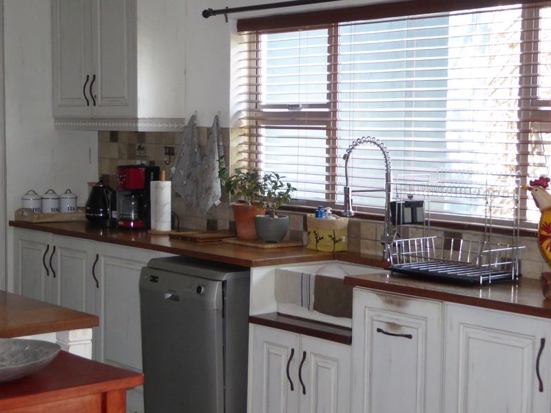 A kitchen featuring white shaker-style cabinetry, wooden countertops, an apron-front sink with a gooseneck faucet, and a tiled backsplash.