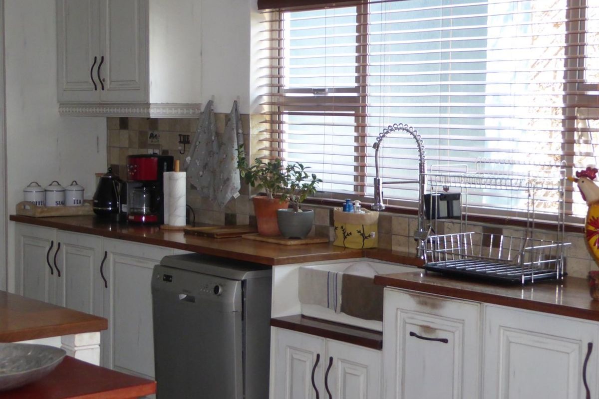 A kitchen featuring white shaker-style cabinetry, wooden countertops, an apron-front sink with a gooseneck faucet, and a tiled backsplash.