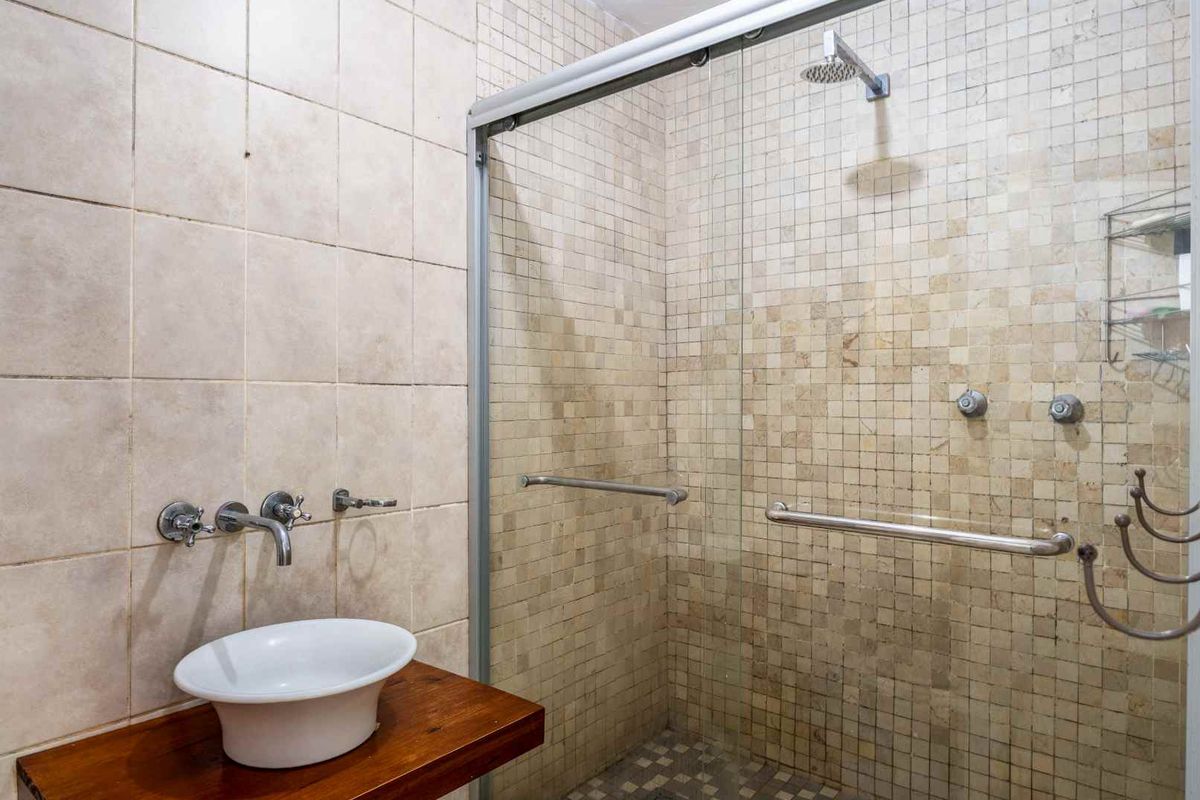 A bathroom featuring a walk-in shower with glass sliding doors, mosaic wall tiling, and a vessel sink mounted on a wooden vanity shelf.