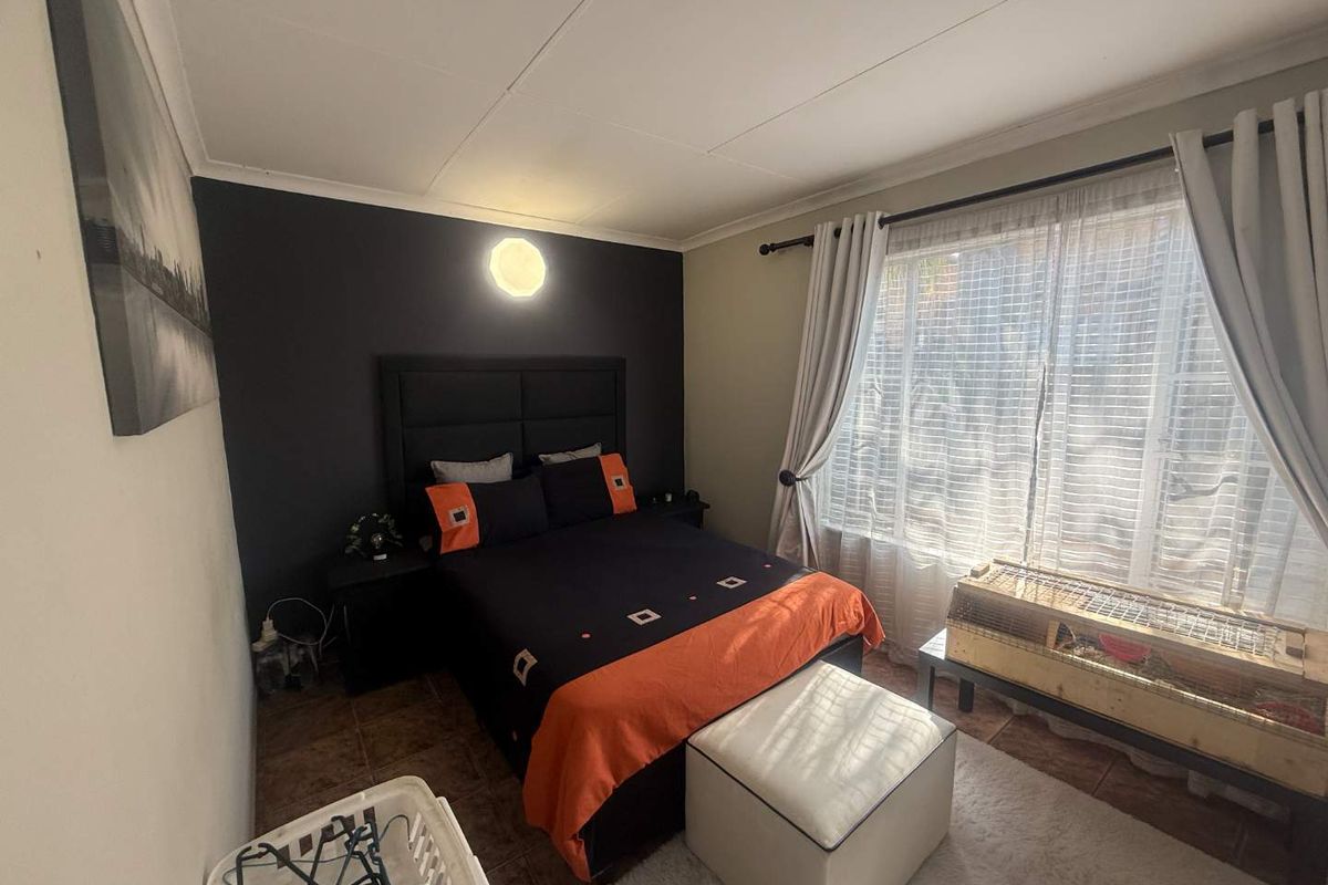 A bedroom featuring tiled flooring and a dark accent wall, providing a functional space with natural light from the window.