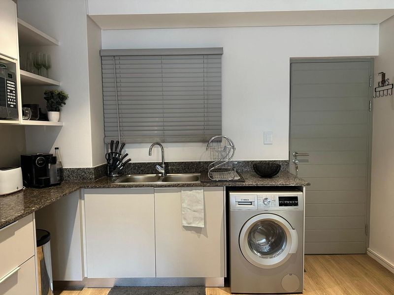 A functional laundry area featuring granite countertops, a double stainless steel sink, built-in cabinetry, and an integrated washing machine.