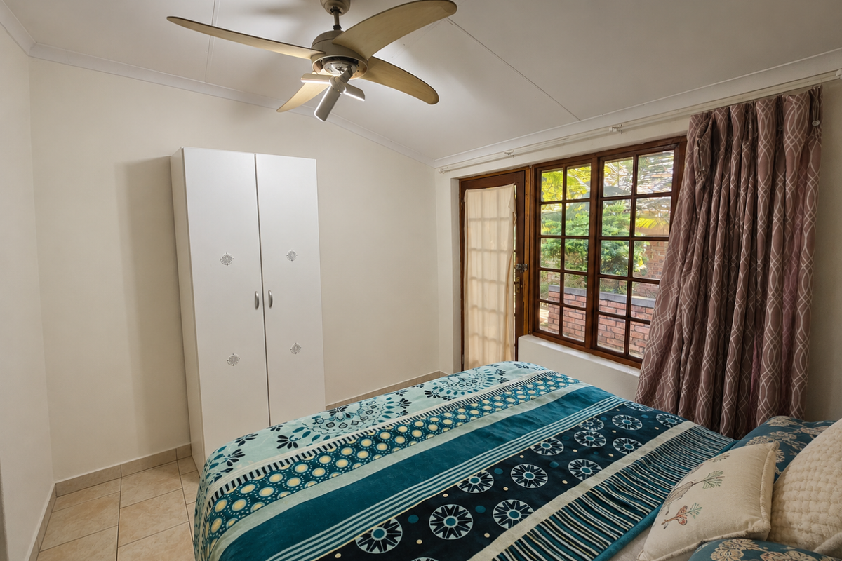 A bedroom featuring tiled flooring, a ceiling fan, a built-in wardrobe, and a wooden-framed window with access to an outdoor area.