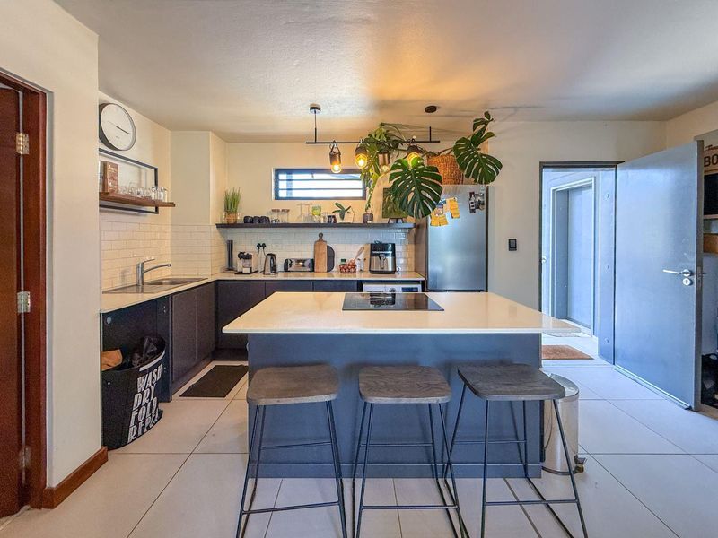 Modern kitchen featuring a central island with a built-in cooktop, subway tile backsplash, sleek cabinetry, and contemporary pendant lighting.