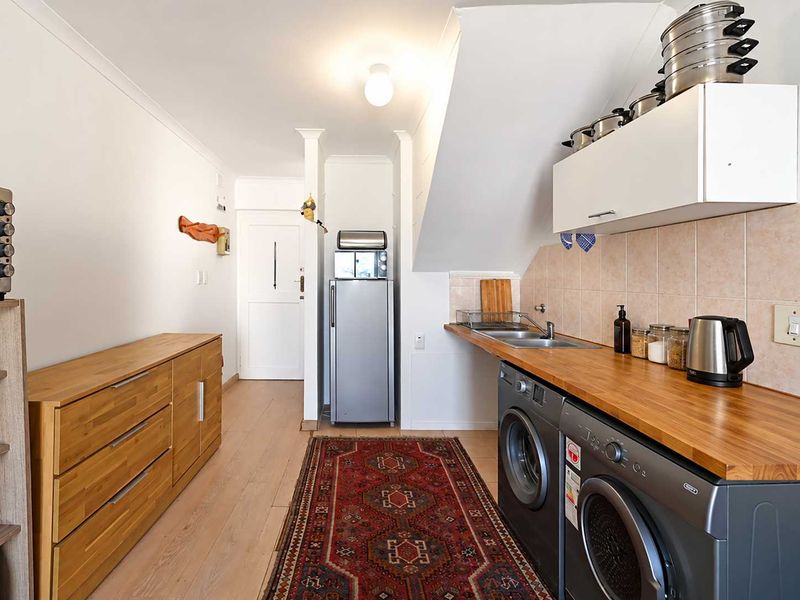 A functional laundry area featuring a wooden countertop, stainless steel sink, tiled backsplash, and built-in cabinetry with space for under-counter appliances.