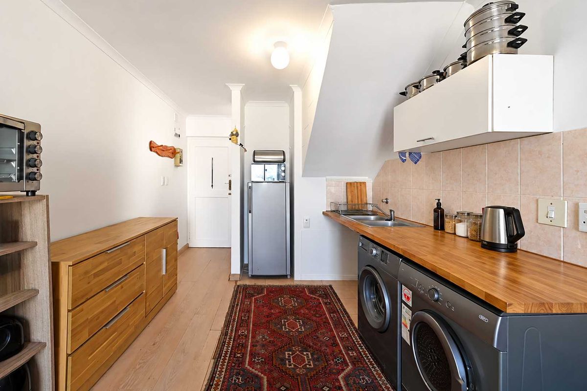 A functional laundry area featuring a wooden countertop, stainless steel sink, tiled backsplash, and built-in cabinetry with space for under-counter appliances.