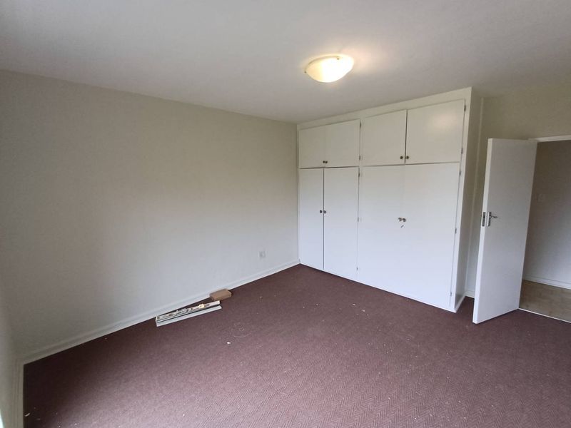 A vacant bedroom featuring built-in white cupboards and carpeted flooring, offering a blank canvas for potential updates and interior design.