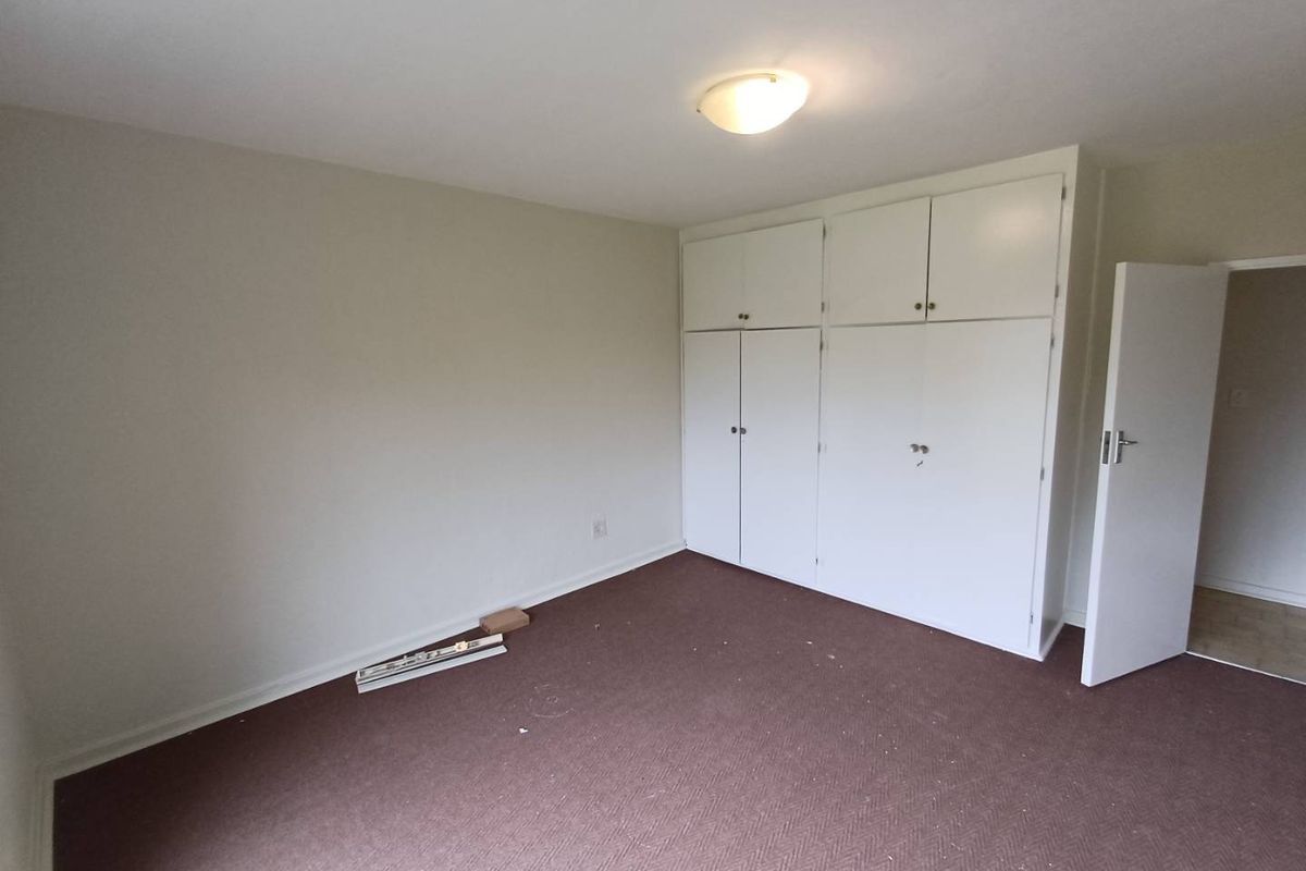 A vacant bedroom featuring built-in white cupboards and carpeted flooring, offering a blank canvas for potential updates and interior design.
