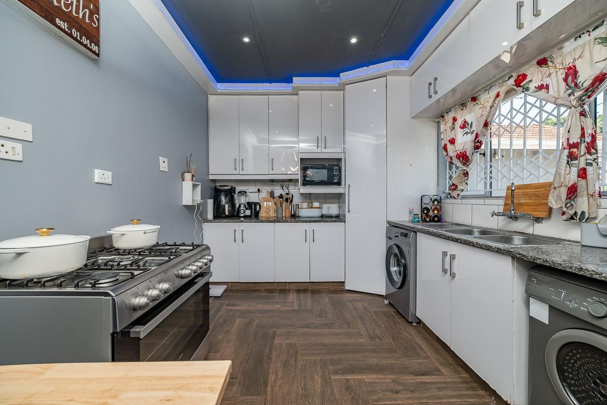 Modern kitchen featuring high-gloss cabinetry, gas stove, integrated microwave, double sink, and stylish herringbone-patterned laminate flooring with ambient cove lighting.