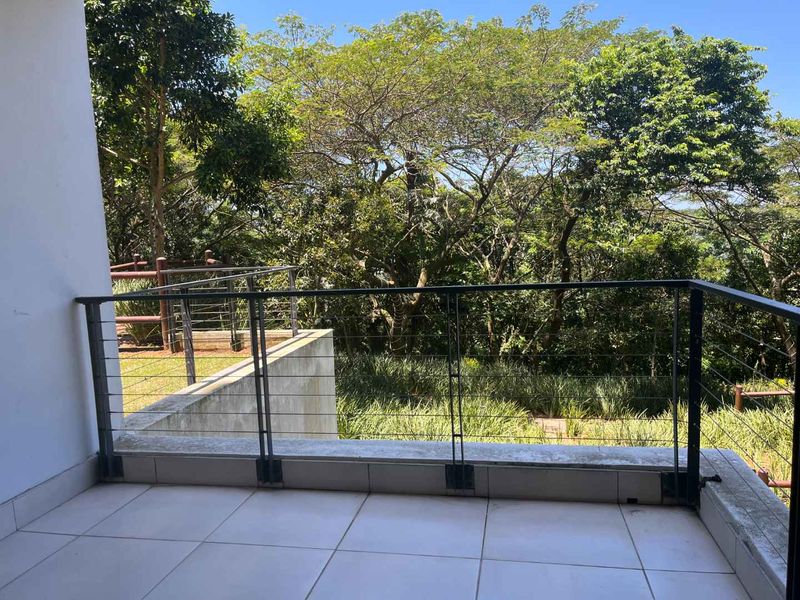 A private balcony featuring tiled flooring and a modern metal cable balustrade, offering a peaceful outlook over the surrounding lush greenery.