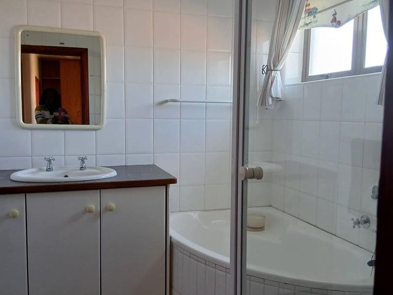 A functional bathroom featuring a vanity with basin, tiled walls, and a shower-over-bath combination with a glass screen.