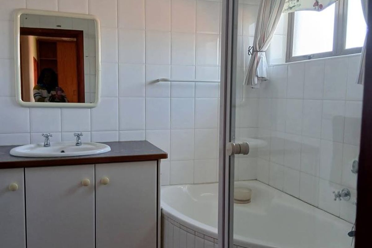 A functional bathroom featuring a vanity with basin, tiled walls, and a shower-over-bath combination with a glass screen.