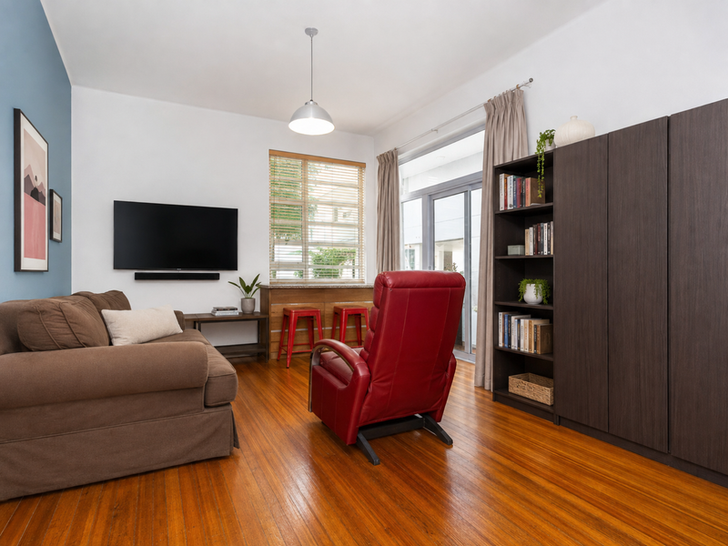 A well-maintained living room featuring polished hardwood flooring, built-in storage cabinetry, and a sliding glass door providing access to an outdoor area.
