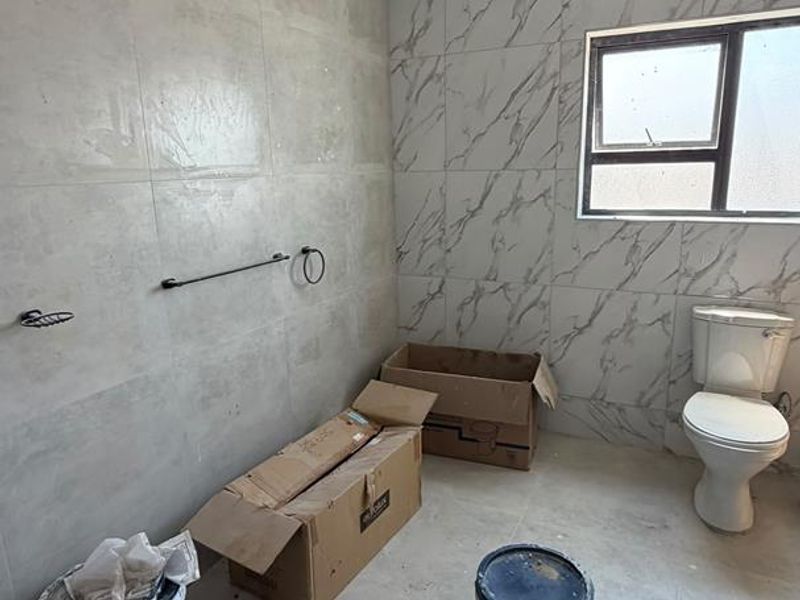 A bathroom currently under renovation featuring modern grey and marble-effect wall tiles, a fitted toilet, and shower plumbing.