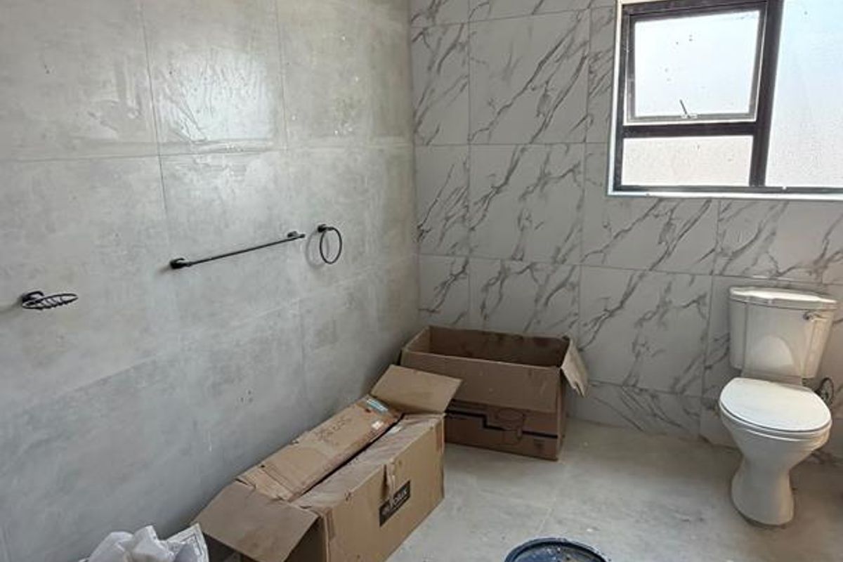 A bathroom currently under renovation featuring modern grey and marble-effect wall tiles, a fitted toilet, and shower plumbing.