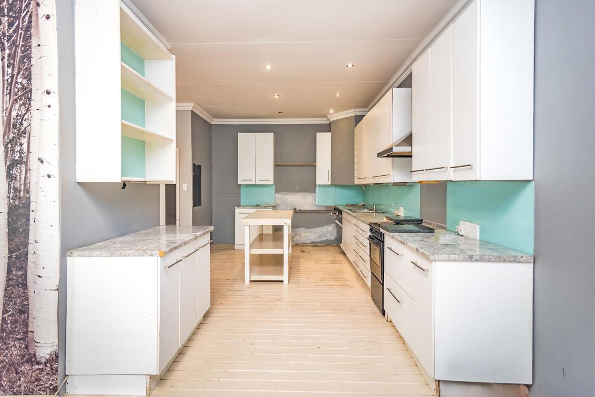 A spacious kitchen featuring white cabinetry, stone countertops, and a glass splashback, currently undergoing renovation with unfinished wall sections and exposed flooring.