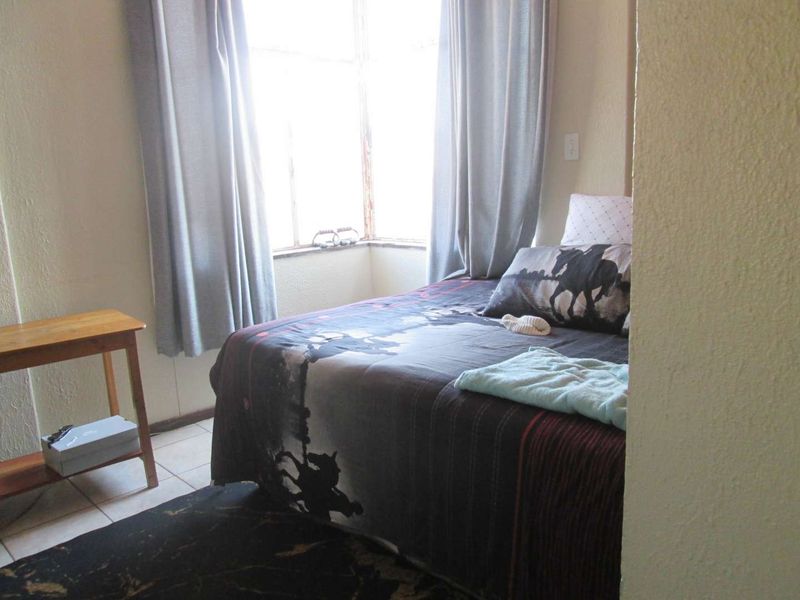 A bedroom featuring tiled flooring and a bay window with natural light, requiring cosmetic updates to the wall finishes and window frames.