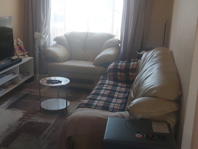 A compact living room area featuring tiled flooring and natural light from a window, providing a functional space for relaxation.
