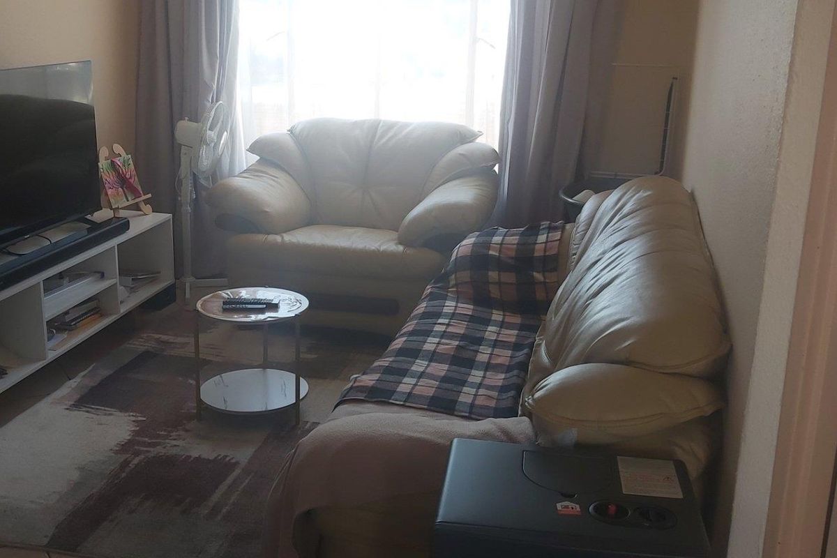 A compact living room area featuring tiled flooring and natural light from a window, providing a functional space for relaxation.