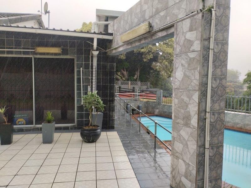 Outdoor pool area featuring a tiled patio, stone-clad structural pillars, and metal safety railings overlooking the swimming pool.