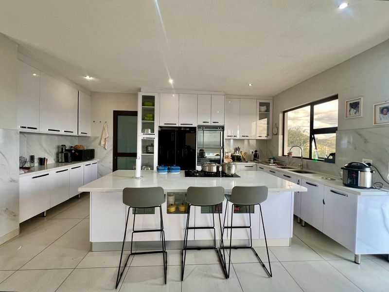 Modern kitchen featuring white cabinetry, a central island with a hob, quartz countertops, and large windows providing natural light.