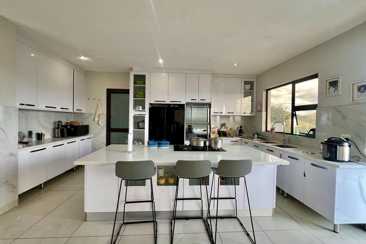 Modern kitchen featuring white cabinetry, a central island with a hob, quartz countertops, and large windows providing natural light.