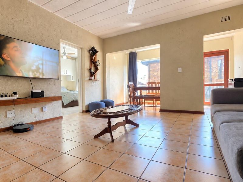 Spacious living room featuring tiled flooring, textured walls, and a ceiling fan, with direct access to an adjoining dining area and bedroom.