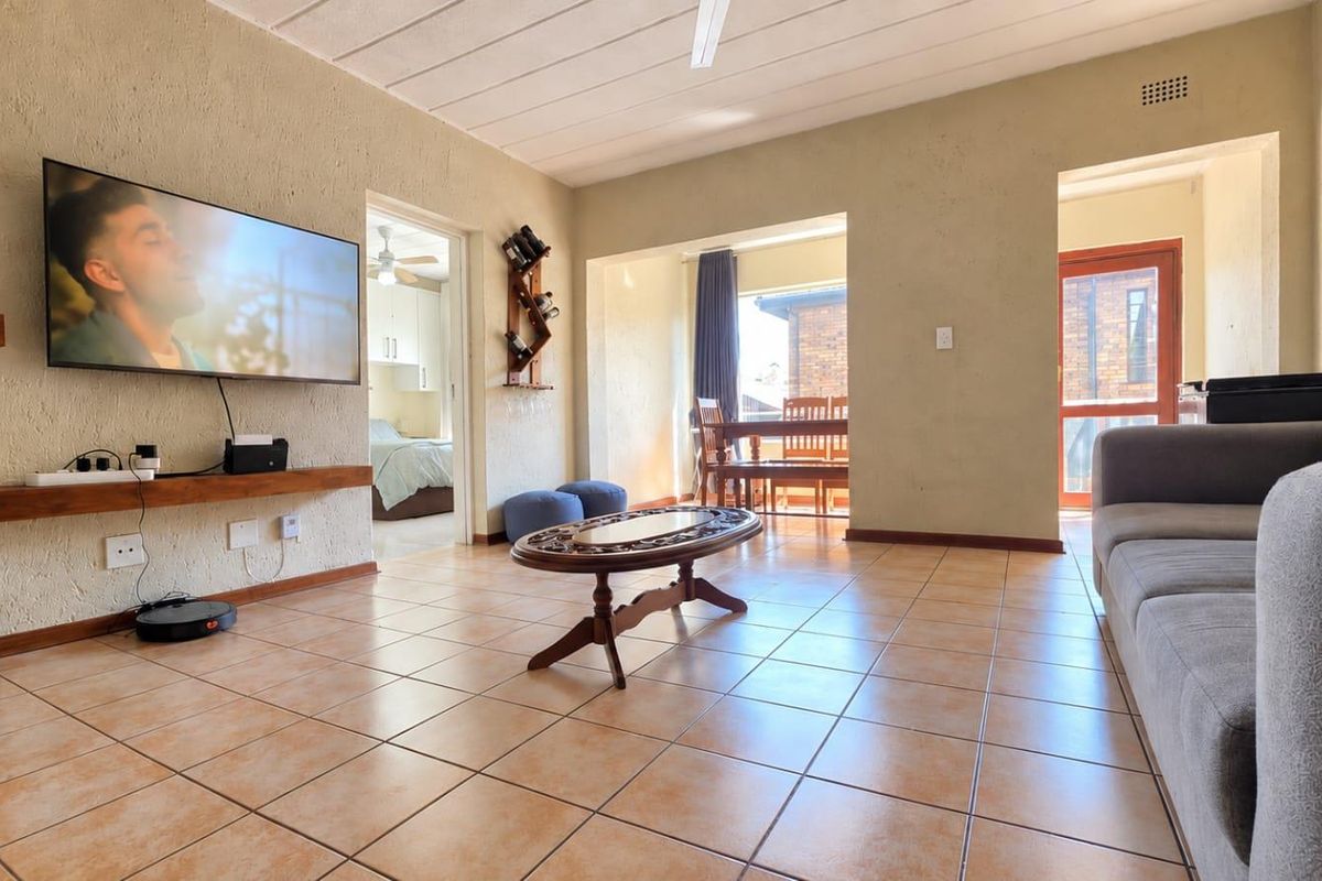 Spacious living room featuring tiled flooring, textured walls, and a ceiling fan, with direct access to an adjoining dining area and bedroom.