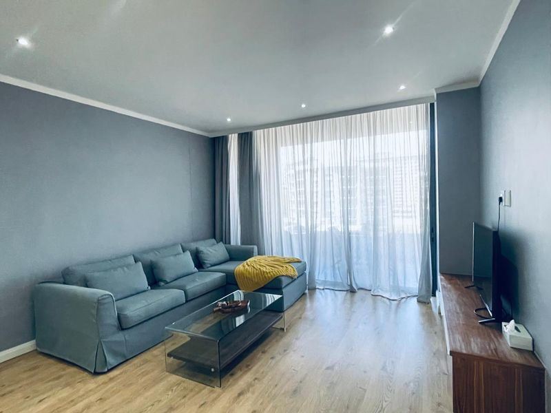 A well-maintained living room featuring laminate flooring, recessed downlighting, and large sliding glass doors providing access to the balcony.
