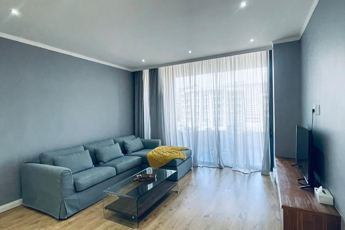 A well-maintained living room featuring laminate flooring, recessed downlighting, and large sliding glass doors providing access to the balcony.