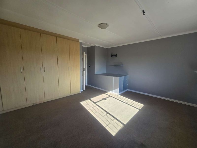 A spacious bedroom featuring neutral grey walls, carpeted flooring, and extensive built-in wooden cupboards for ample storage.