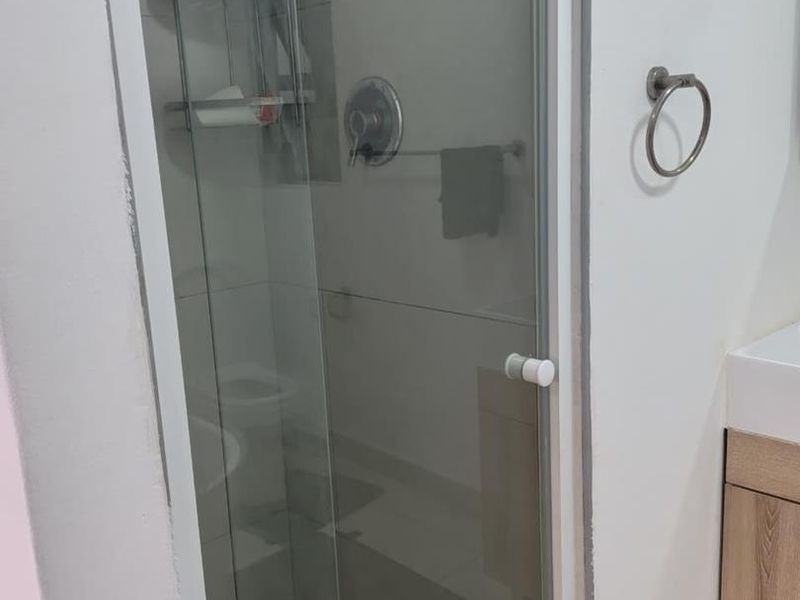 A functional bathroom featuring a glass-enclosed shower, vanity cabinet, and tiled flooring, presenting a clean and practical layout.