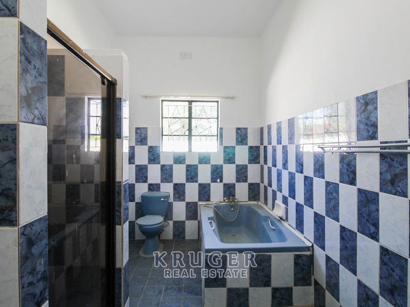 A dated bathroom featuring blue and white checkered wall tiles, a built-in bathtub, a separate shower enclosure, and a blue toilet.