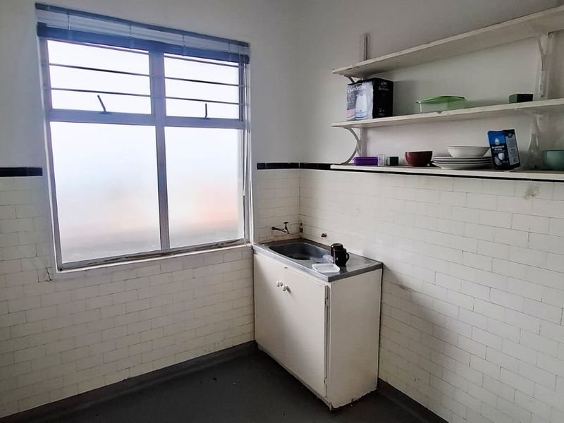 A functional scullery or utility area featuring a single basin sink, wall-mounted shelving, and tiled splashbacks, requiring cosmetic updates to improve its condition.