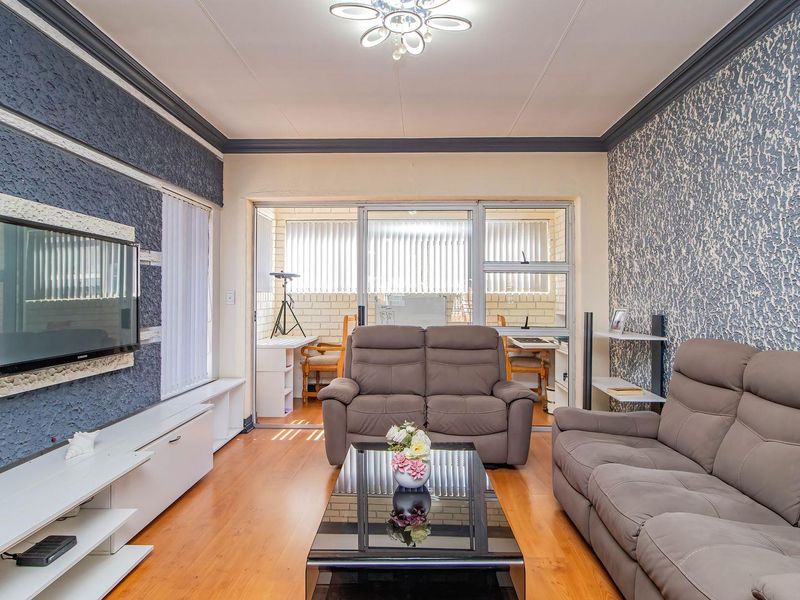 A living room featuring laminate flooring, textured accent walls, crown molding, and sliding glass doors leading to an enclosed patio area.