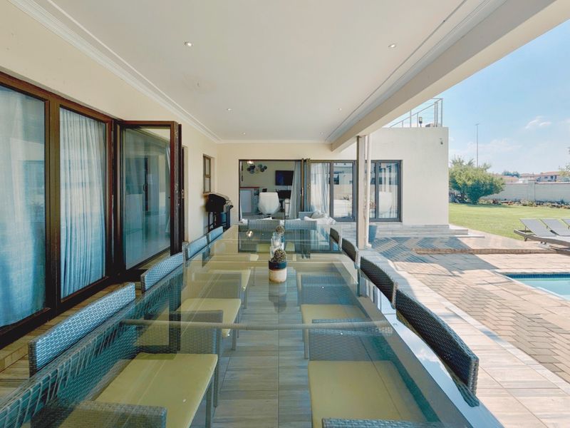 Spacious covered patio featuring tiled flooring and bi-fold glass doors, providing seamless indoor-outdoor flow to the pool area and garden.