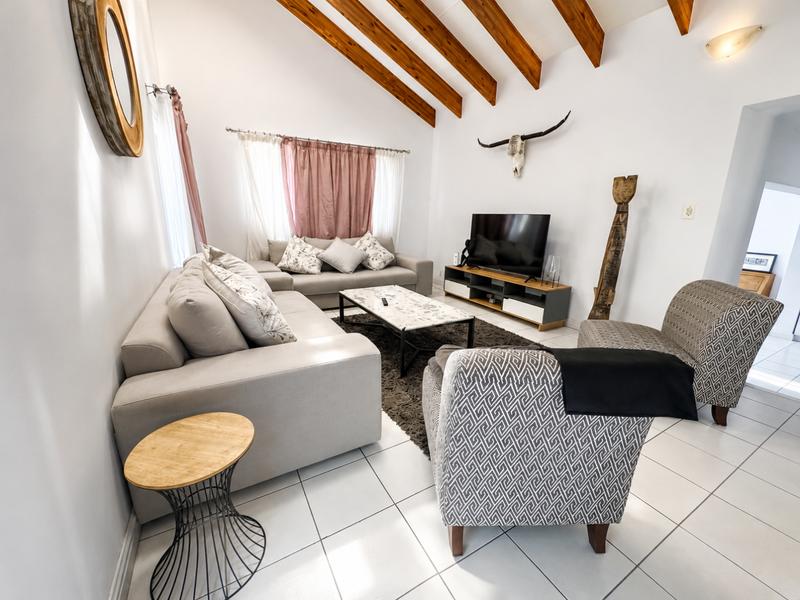 A bright living room featuring a vaulted ceiling with exposed timber beams and clean tiled flooring, creating an open and airy atmosphere.
