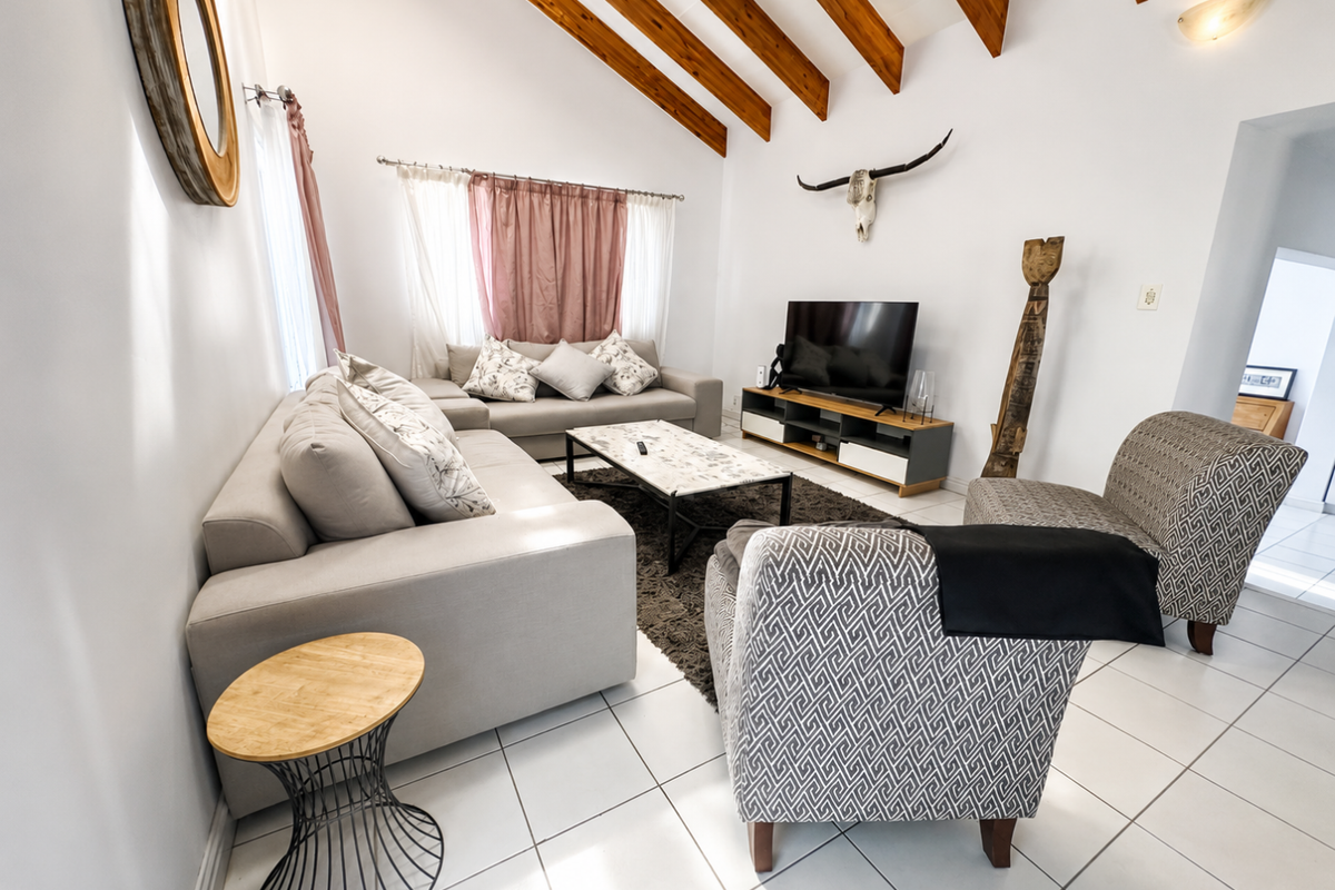 A bright living room featuring a vaulted ceiling with exposed timber beams and clean tiled flooring, creating an open and airy atmosphere.