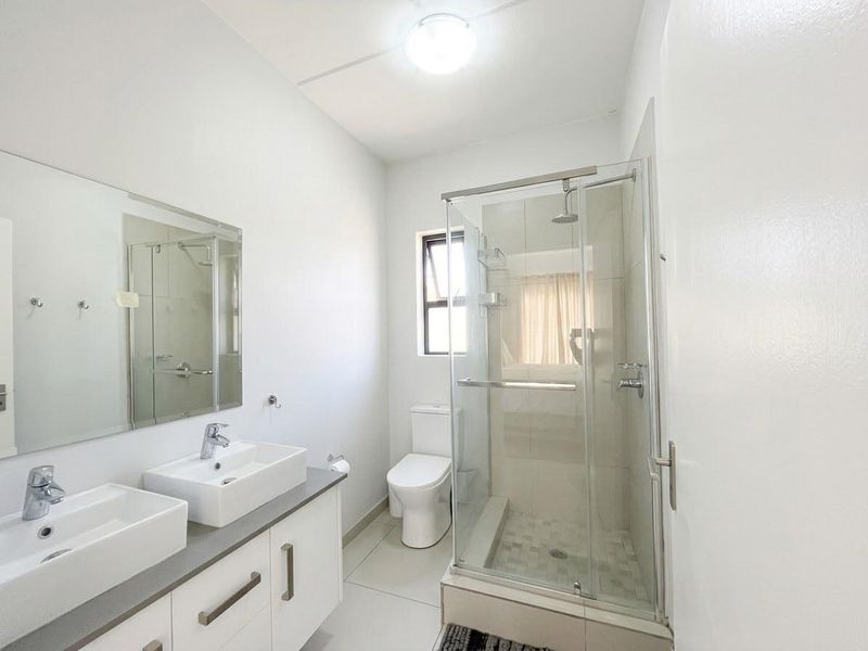 A clean, modern bathroom featuring a double vanity, glass-enclosed shower, and neutral tiling, offering a bright and functional space.