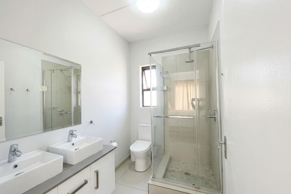 A clean, modern bathroom featuring a double vanity, glass-enclosed shower, and neutral tiling, offering a bright and functional space.