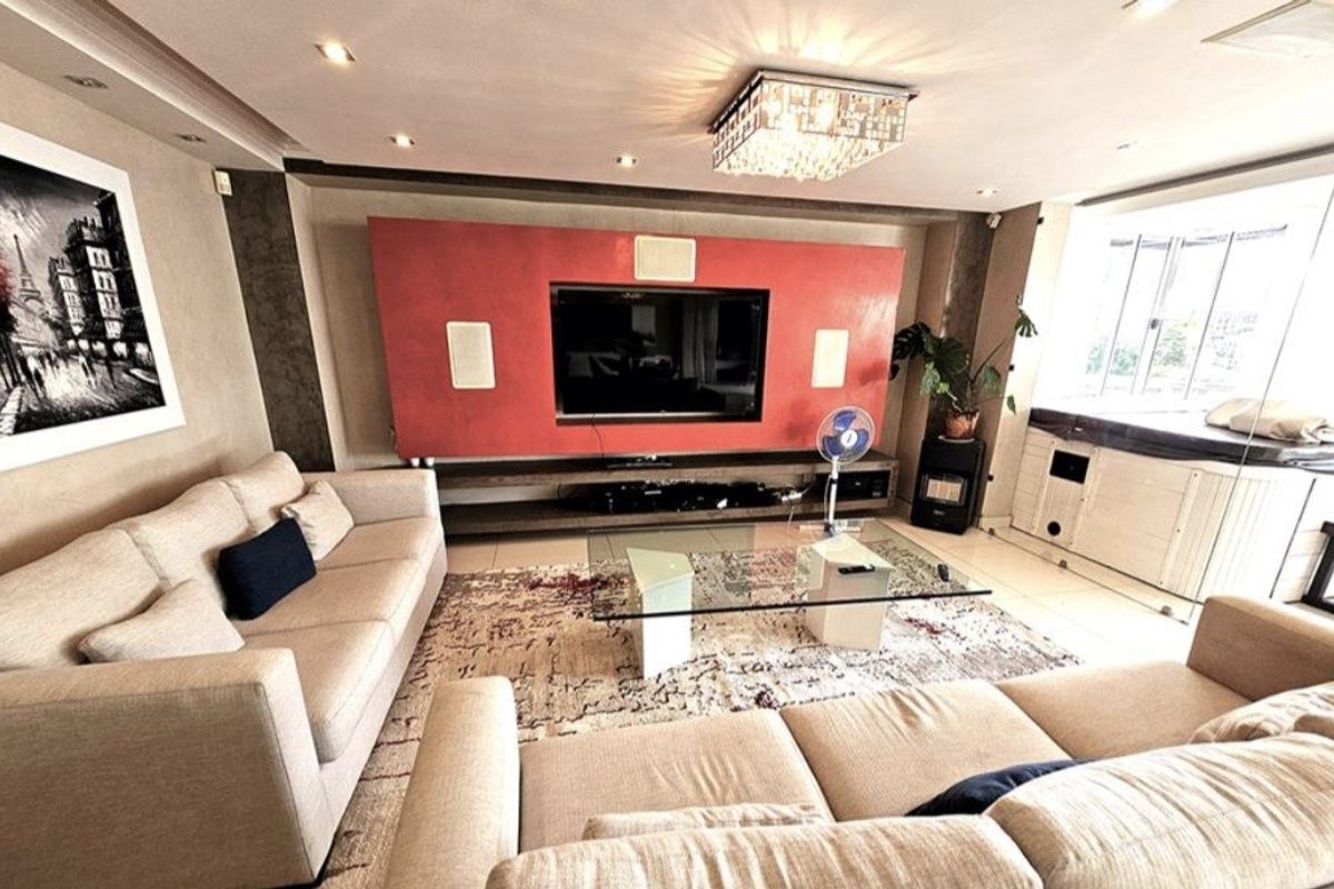 Spacious living room featuring a prominent built-in media wall, recessed ceiling lighting, a decorative crystal chandelier, and neutral tiled flooring.