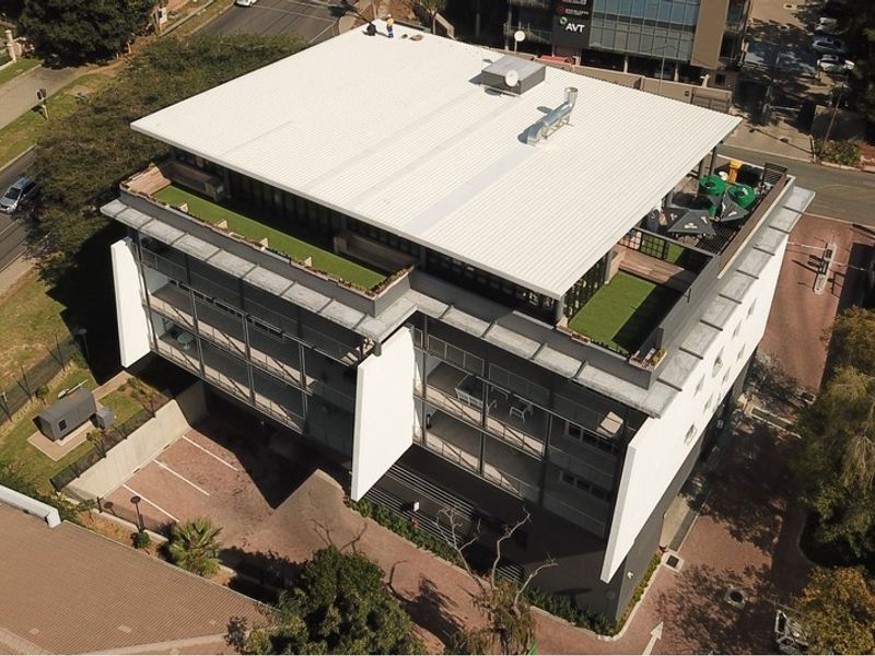 Aerial view of a modern multi-story office building featuring a rooftop terrace with artificial turf and an adjacent paved parking area.
