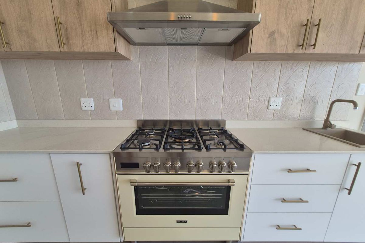 Modern kitchen featuring a freestanding Elba gas stove, stainless steel extractor fan, stone countertops, and a combination of white and wood-grain cabinetry.