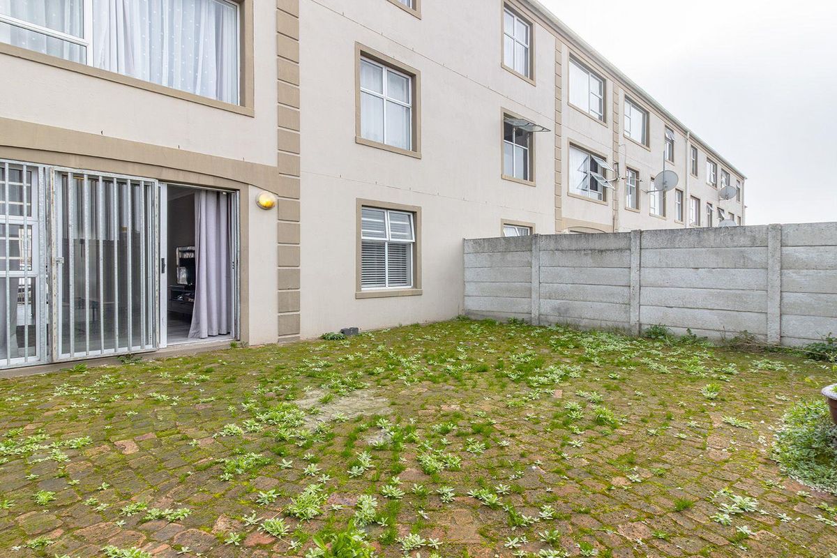 Rear exterior view of an apartment building featuring a private paved courtyard enclosed by a precast concrete boundary wall.