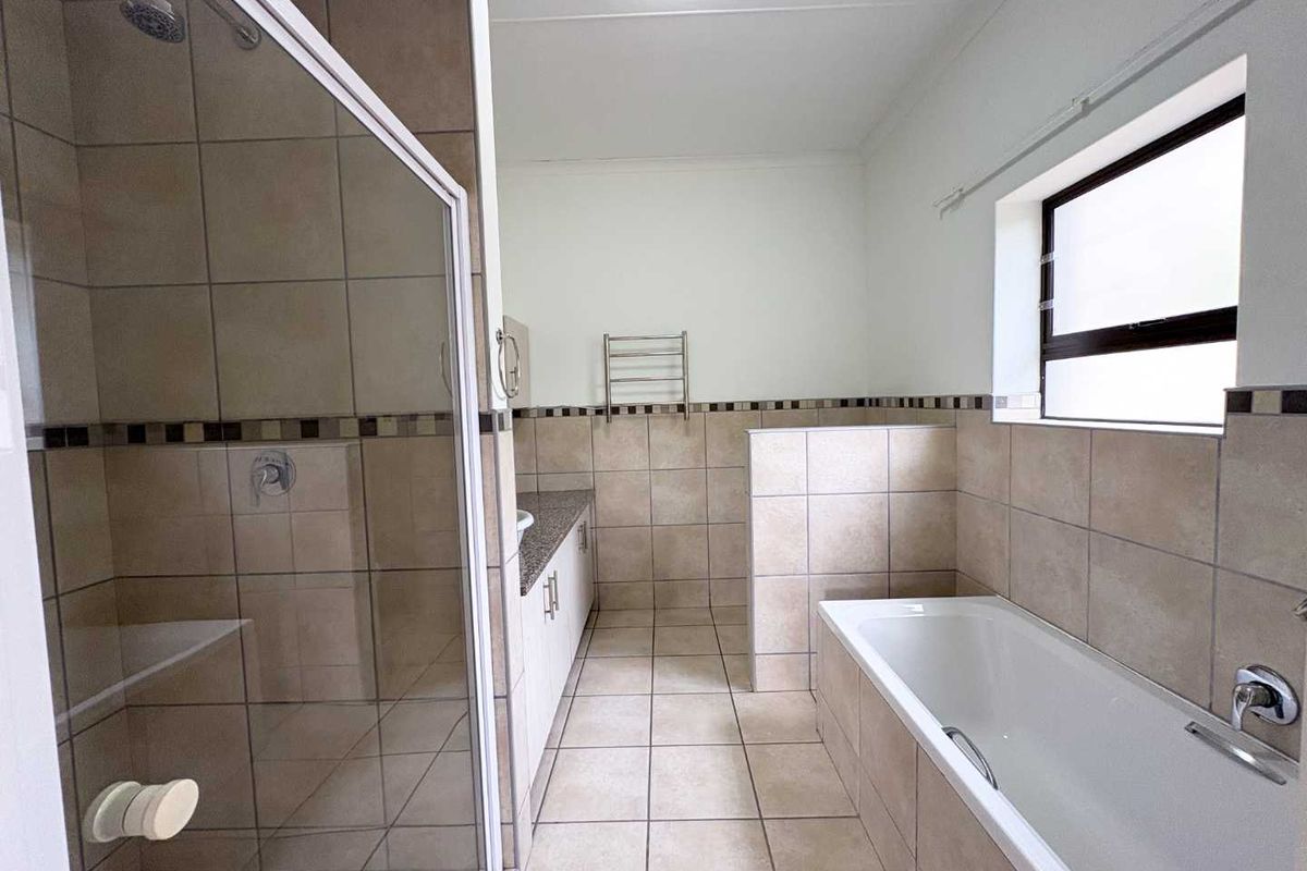 A functional bathroom featuring a glass-enclosed shower, a separate bathtub, a vanity with granite countertop, and a wall-mounted heated towel rail.