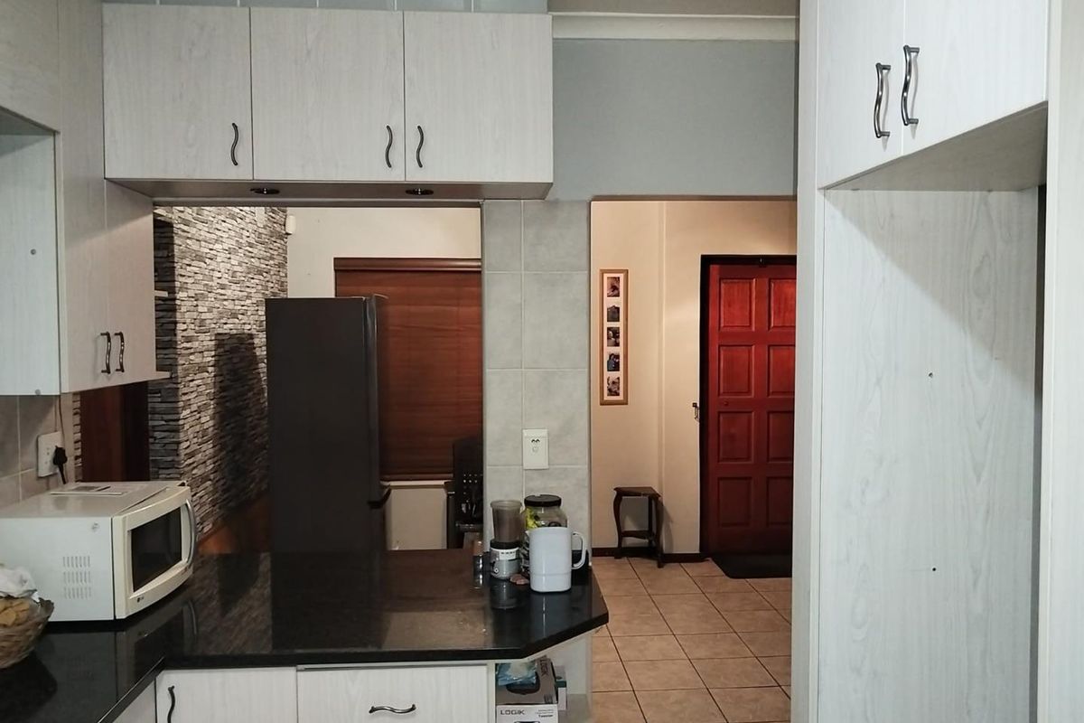 A functional kitchen featuring light wood-grain cabinetry, dark granite countertops, and tiled flooring, with an open-plan layout leading to the entrance hall.