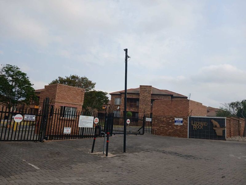 The entrance to Leopard Rock apartment complex featuring a secure gated access point, brick perimeter walls, and a paved driveway.
