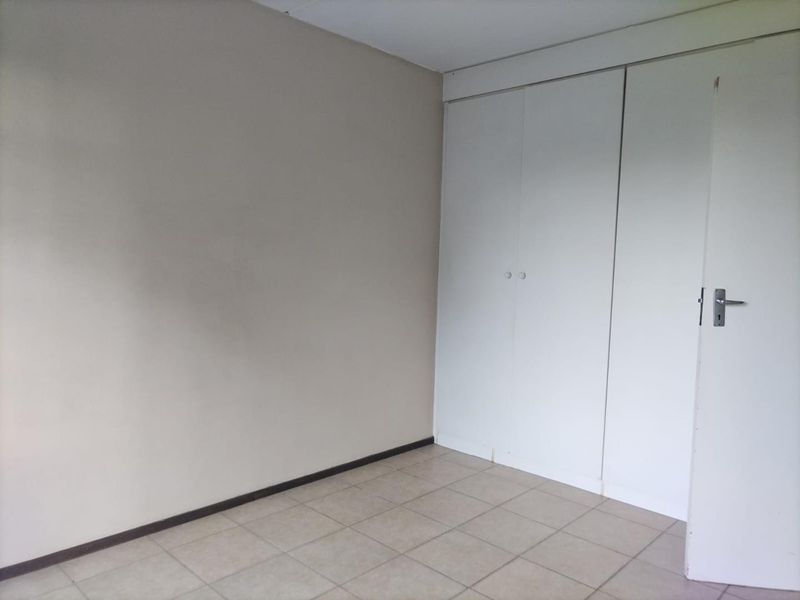 An empty bedroom featuring neutral tiled flooring and built-in cupboards, providing a blank canvas for personalization.